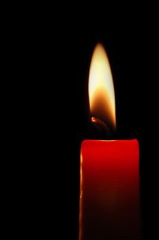 Burning red candle on black background