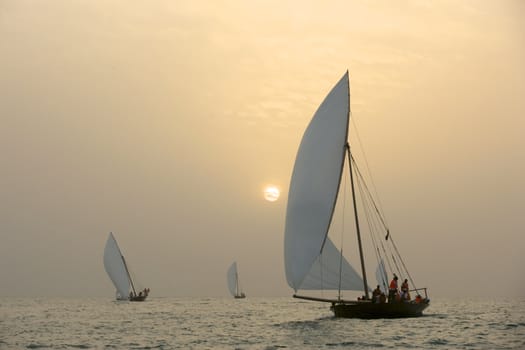 Traditional Dhows sailing in the Arabian Gulf, off Dubai, at sunset.