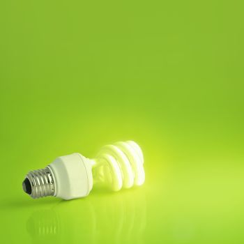 A vibrant presentation of a modern energy-saving lightbulb lit on a lush green background.  Plenty of copyspace, ideal for ecology, energy concepts or imagination and marketing pitches