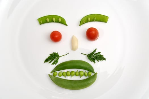 Vegetable face made of peas, parsley, tomato and garlic on a white plate