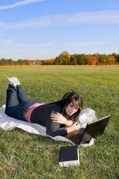 A young student using her laptop computer while laying in the grass on a nice day.