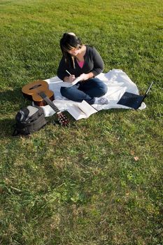 A young musician writing in her notebook while sitting in the grass on a nice day.