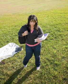 A young woman walking on campus on a nice day with her books and backpack.