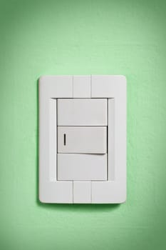 White light switch against a green wall.