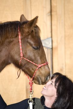 A cute sorrel (chestnut) foal nuzzling the face of an attractive, dark-haired woman.