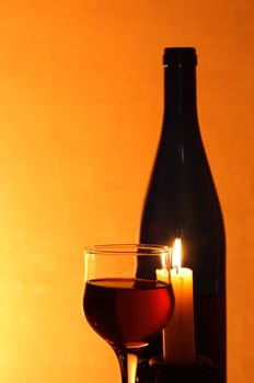 Wineglass near bottle of red wine and candle on nice red background