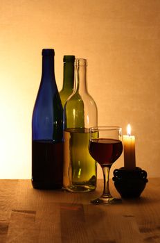 Three bottles of red and white wine wineglass candle on wooden background