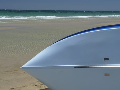 A blue boat lies on its side on the beach