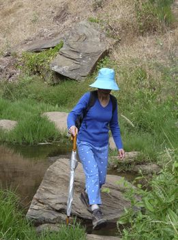 A middle aged woman strides out over a creek