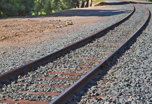 Brightly lit railroad track curve with gray gravel on either side