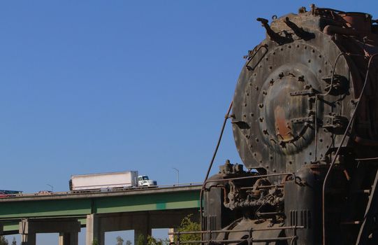 Old rusted train engine  against background of elevated highway with truck