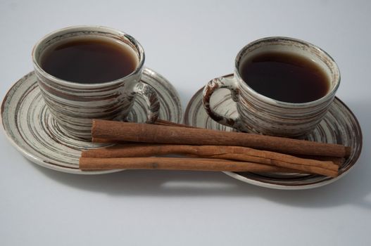 Two cups of tea  and cinnamon sticks on the white background .