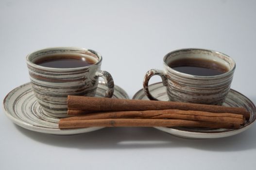 Two cups of tea  and cinnamon sticks on the white background .