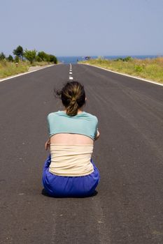 Young woman sitting in middle of road with back to camera