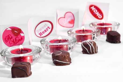 Candles, chocolates and love note cards in a line on white background
