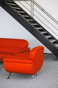 Metal stairs above  red sofa in minimalistic interior