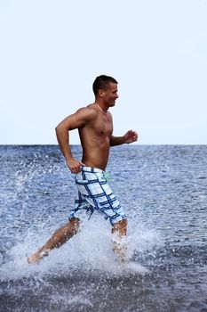 Athletic Handsome Man Running In Water and Creating Splashes