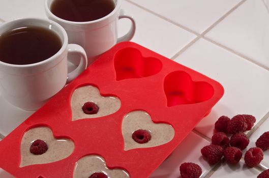 Tea with preparation of muffins in heart shaped pan with raspberries