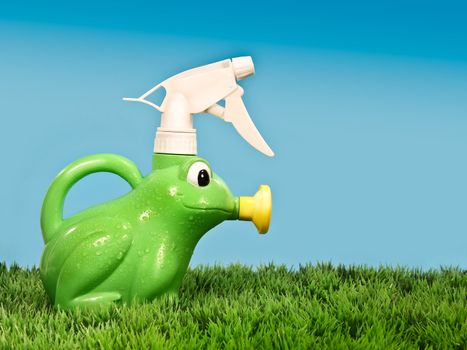 Child's spray bottle on grass with blue background