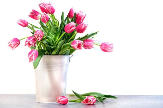 Pink tulips in white metal container against kitchen tiles 