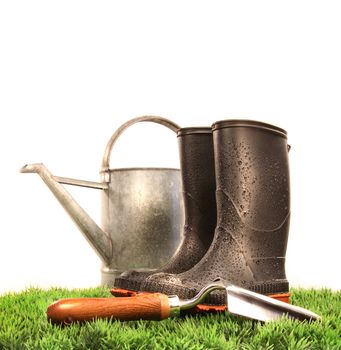 Garden boots with tool and watering can on grass