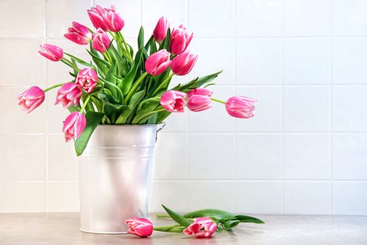 Pink tulips in white metal container against kitchen tiles 