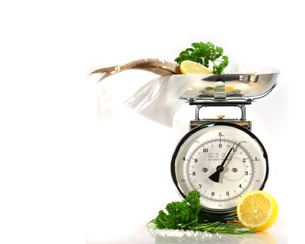Weight scale, fish,lemon on parchment paper against white