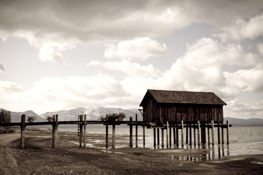 Landscape of wooden jetty extending out, dramatic clouds and mountains in background