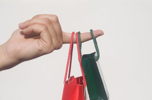 Finger holding two small shopping bags against white background