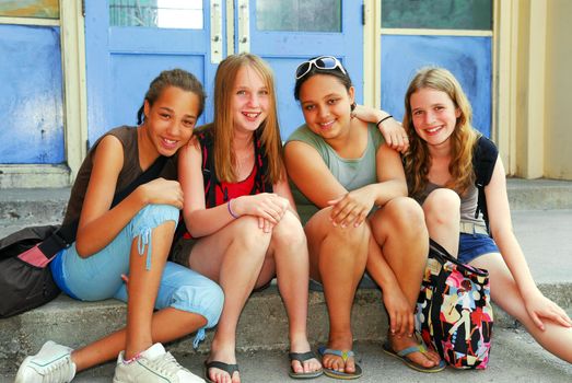 Portrait of a group of young smiling school girls sitting on steps near school building