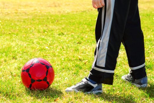 Young boy playing with red soccer boy outside