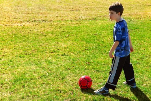 Young boy playing with red soccer boy outside