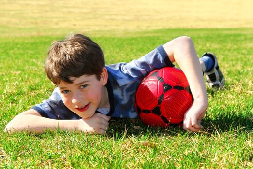 Young cute happy boy lying on grass with red soccer ball 