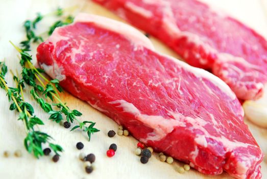 Two raw new york steaks on cutting board with thyme and peppercorns