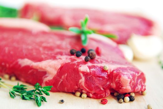 Two raw new york steaks on cutting board with thyme peppercorns and garlic