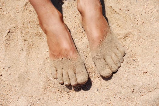 boy's feet in yellow fine sand on beach closeup