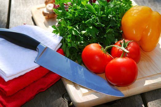 Assorted fresh vegetables on cutting board on rustic table with a chef knife
