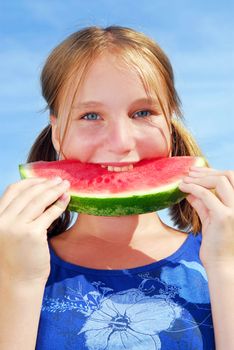 Young girl biting into a slice of watermelon on blue sky background