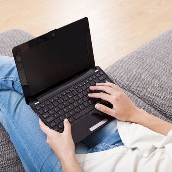 Young woman at home seated on sofa and working with a laptop