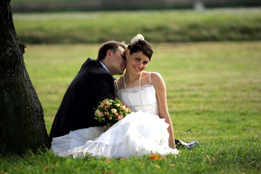 Newlywed couple kissing in summer under shade of tree.