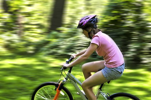 Portrait of a teenage girl riding a bicycle in summer park outdoors