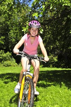 Portrait of a teenage girl riding a bicycle in summer park outdoors