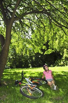 Teenage girl relaxing under green tree with her bicycle