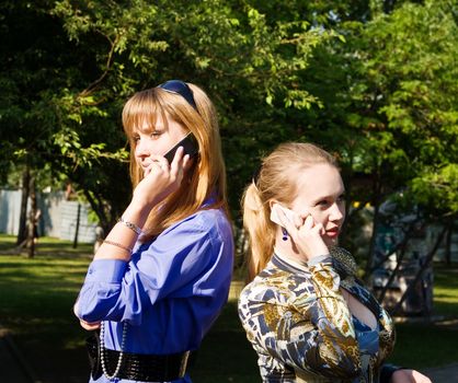 Beaty young women talks from cellular phones on the park