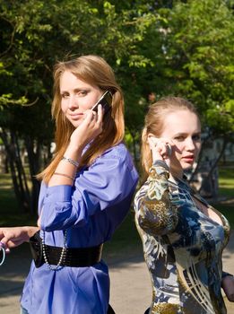 Beaty young women talks from cellular phones on the park