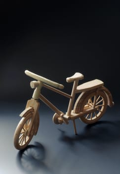Bicycle small wooden toy model. Dark matt background with wheel shadows.
