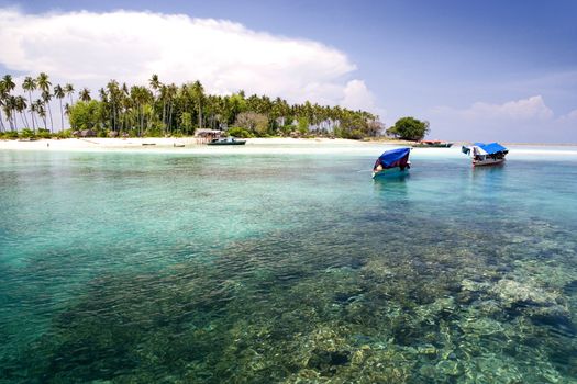 Image of a remote Malaysian tropical island with deep blue skies, crystal clear waters, boats and coconut trees.