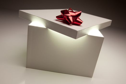 Gift Box with Red Bow Lid Revealing Very Bright Contents on a Gradated Background.