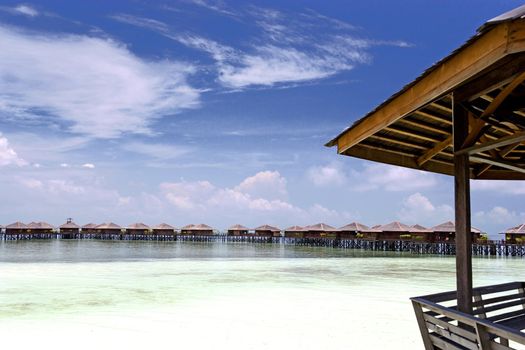 Image of huts on stilts on a remote Malaysian tropical island with deep blue skies and crystal clear waters.