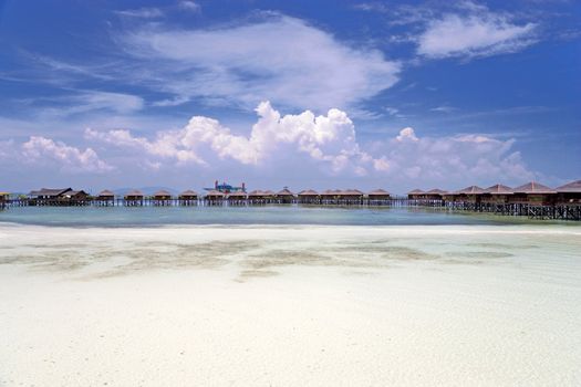 Image of chalets on stilts on a remote Malaysian tropical island with deep blue skies, white sand and crystal clear waters.